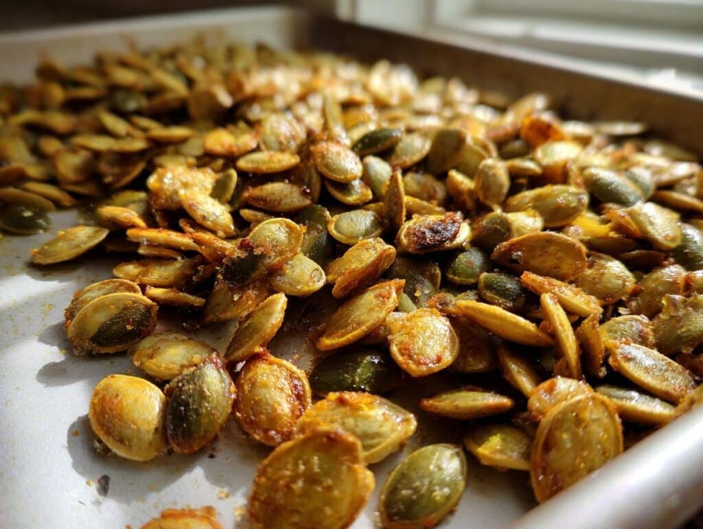 Close-up shot of freshly roasted Sea Salt Olive Oil Roasted Pumpkin Seeds on a baking sheet, glistening with oil and spices.